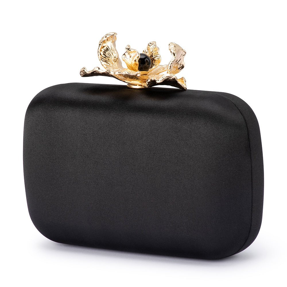 Black satin clutch turned to a three-quarter view, the gold orchid clasp on top