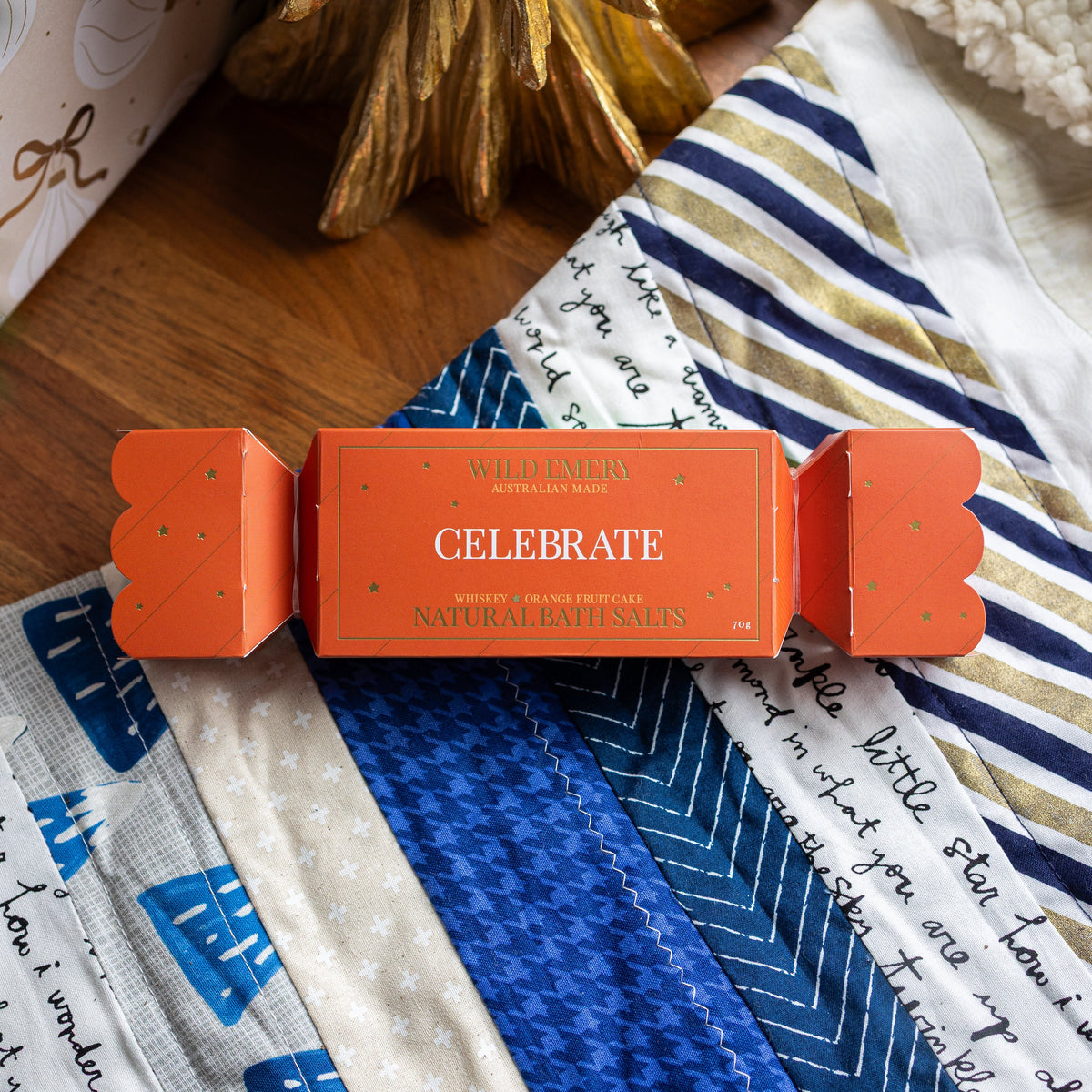 Orange Celebrate bath salt bon bon, shaped like a Christmas cracker, on a patchwork quilt.