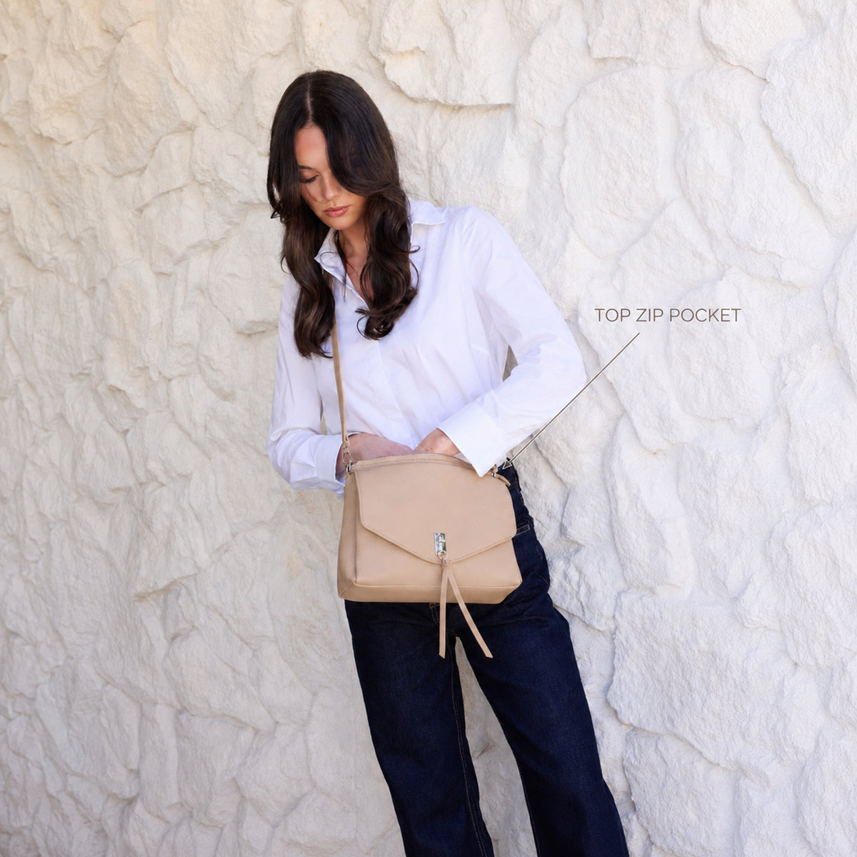The biscuit bag worn across the body, with a label pointing to its top zip pocket.