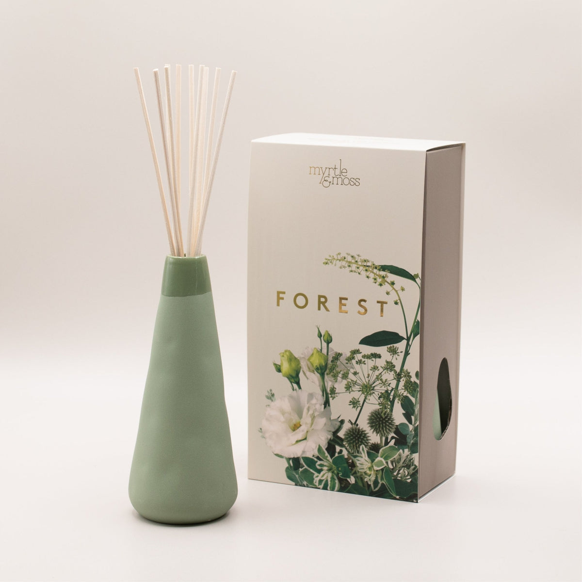 The sage green ceramic vase with its reeds beside the Forest box, seen from the side.