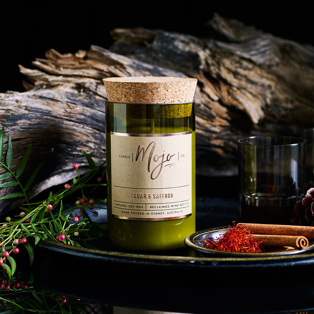 Cedar & Saffron candle on a dark plate with saffron threads, cinnamon, driftwood and red berries