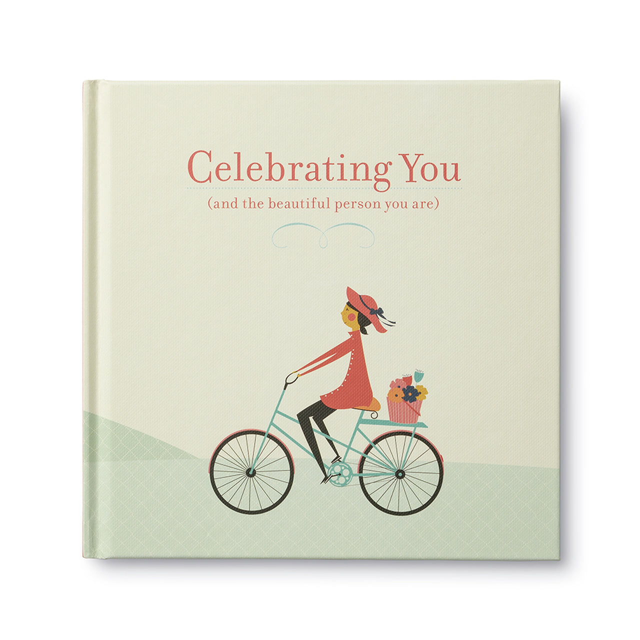 Cream hardcover titled Celebrating You with a woman cycling and a small dog in the basket