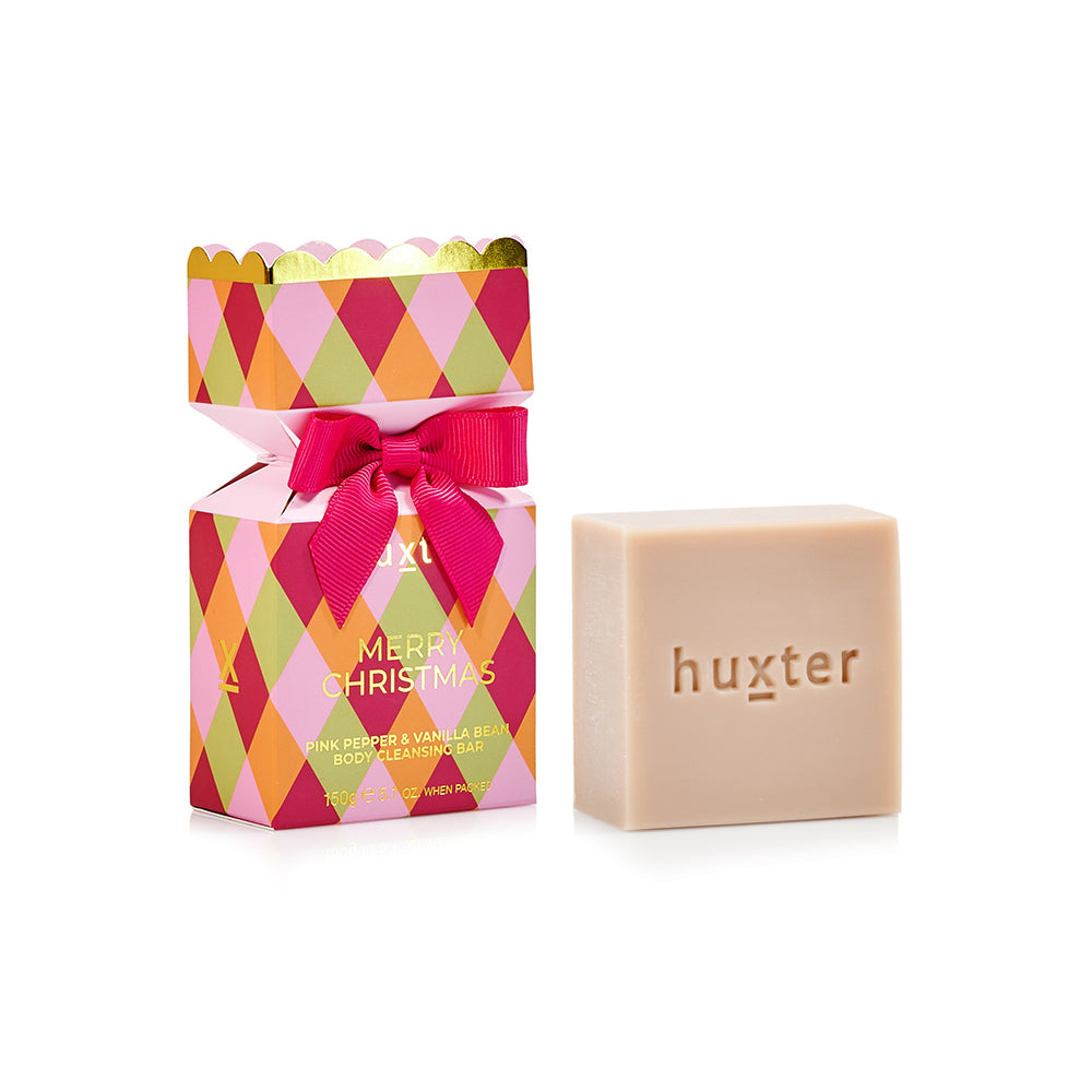 Huxter bon bon box with pink, orange and green diamonds, pink bow and gold scalloped top, beside the pale cleansing bar stamped huxter.