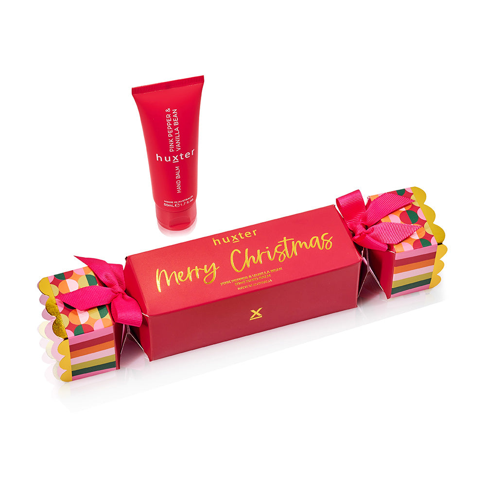 Red Huxter Christmas cracker box printed Merry Christmas in gold, tied with pink ribbon, with the red 50 mL hand balm tube.