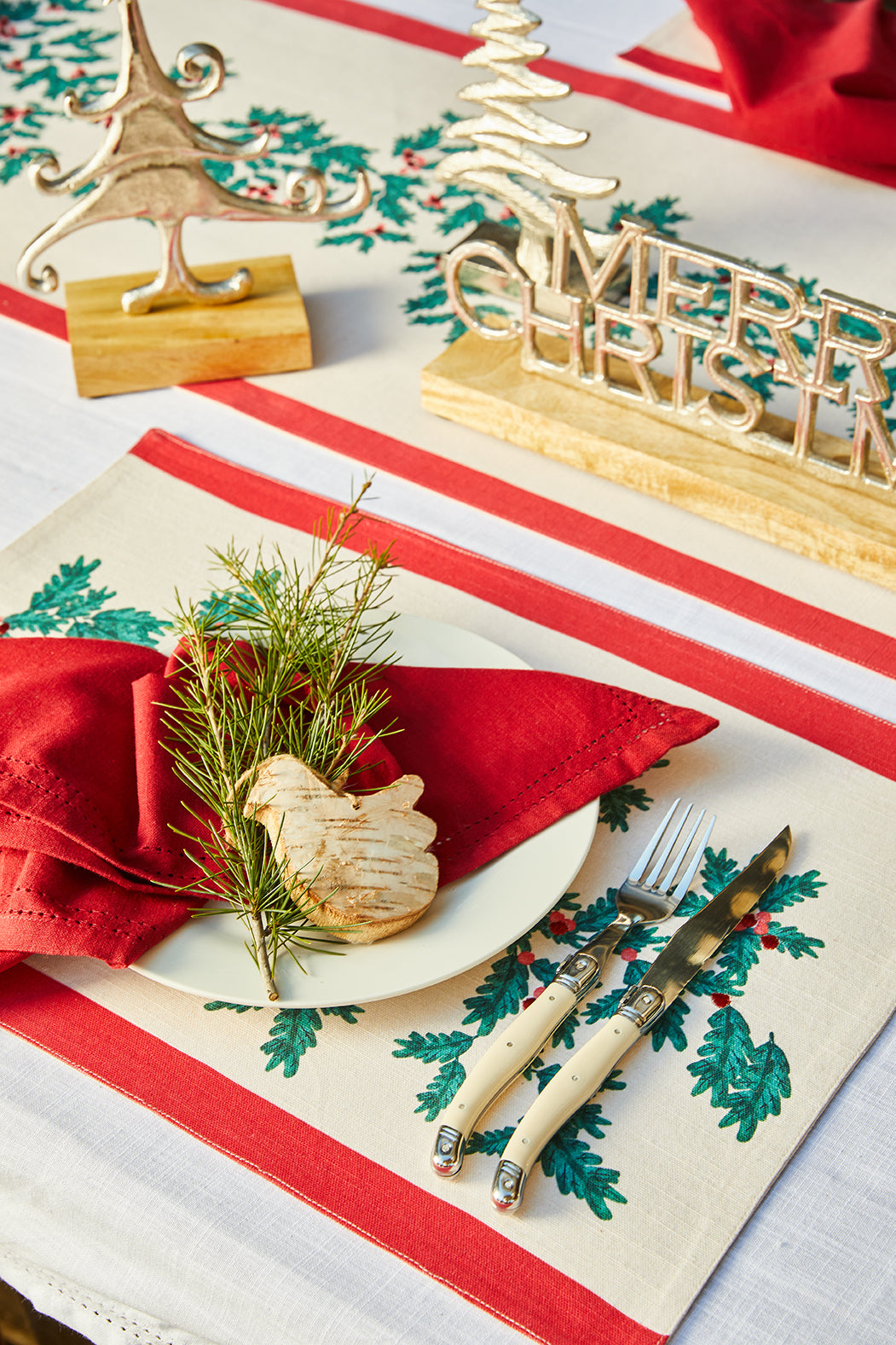 Christmas Foliage placemat under a white plate with a red napkin and cutlery on a Christmas table