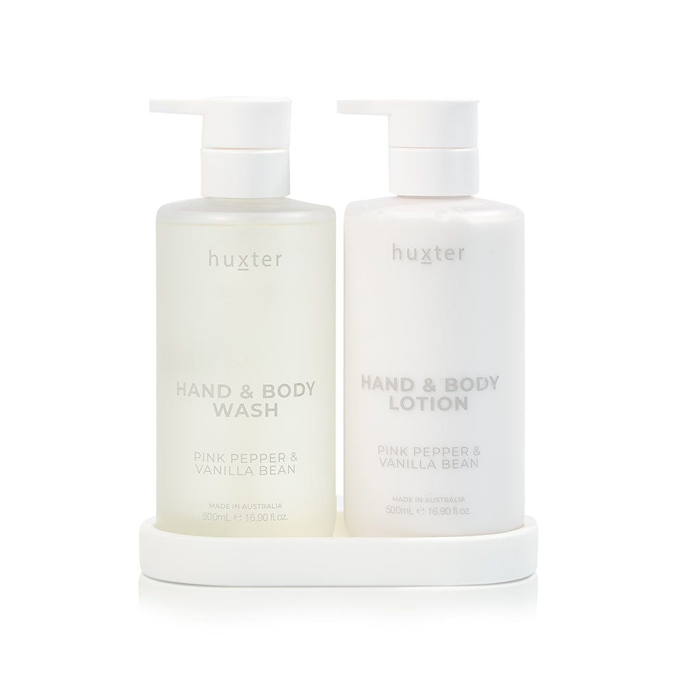 A frosted Huxter hand and body wash bottle and a white lotion bottle, Pink Pepper & Vanilla Bean, with white pumps on a white silicone tray.