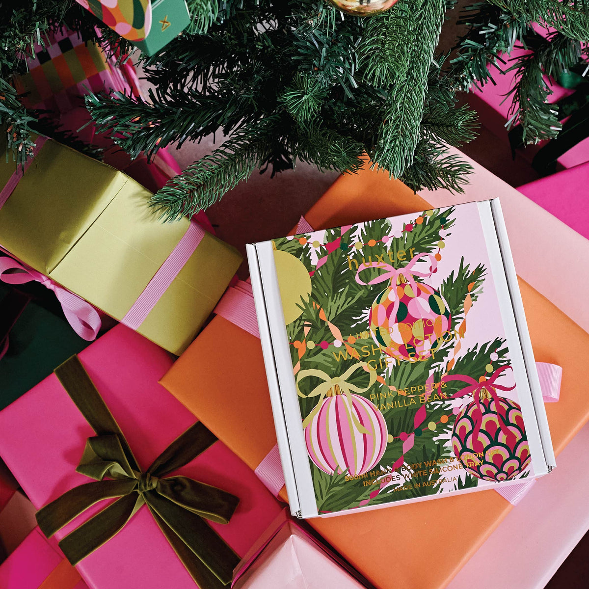 The Huxter Christmas wash and lotion gift box among wrapped presents under a Christmas tree.
