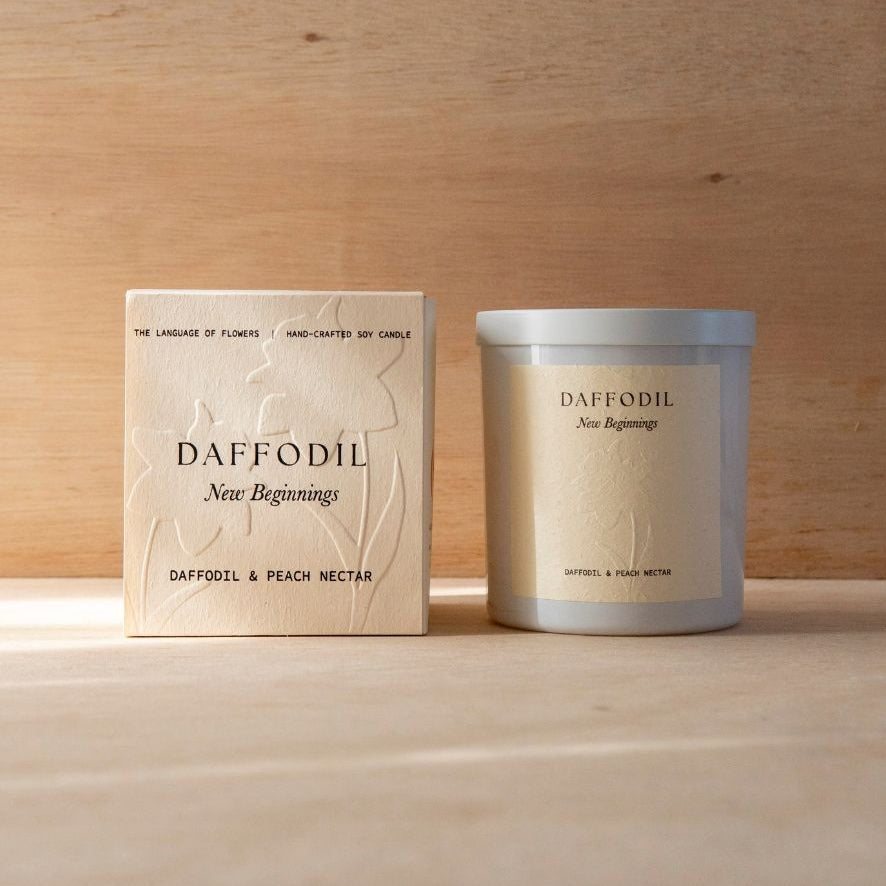 The Daffodil candle in its white vessel beside its cream box.