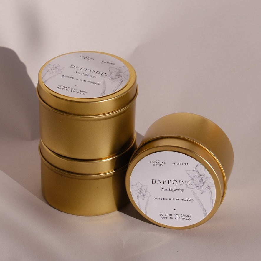 Three gold Daffodil travel tins, one tipped forward to show its lid label with a drawing of the daffodil.
