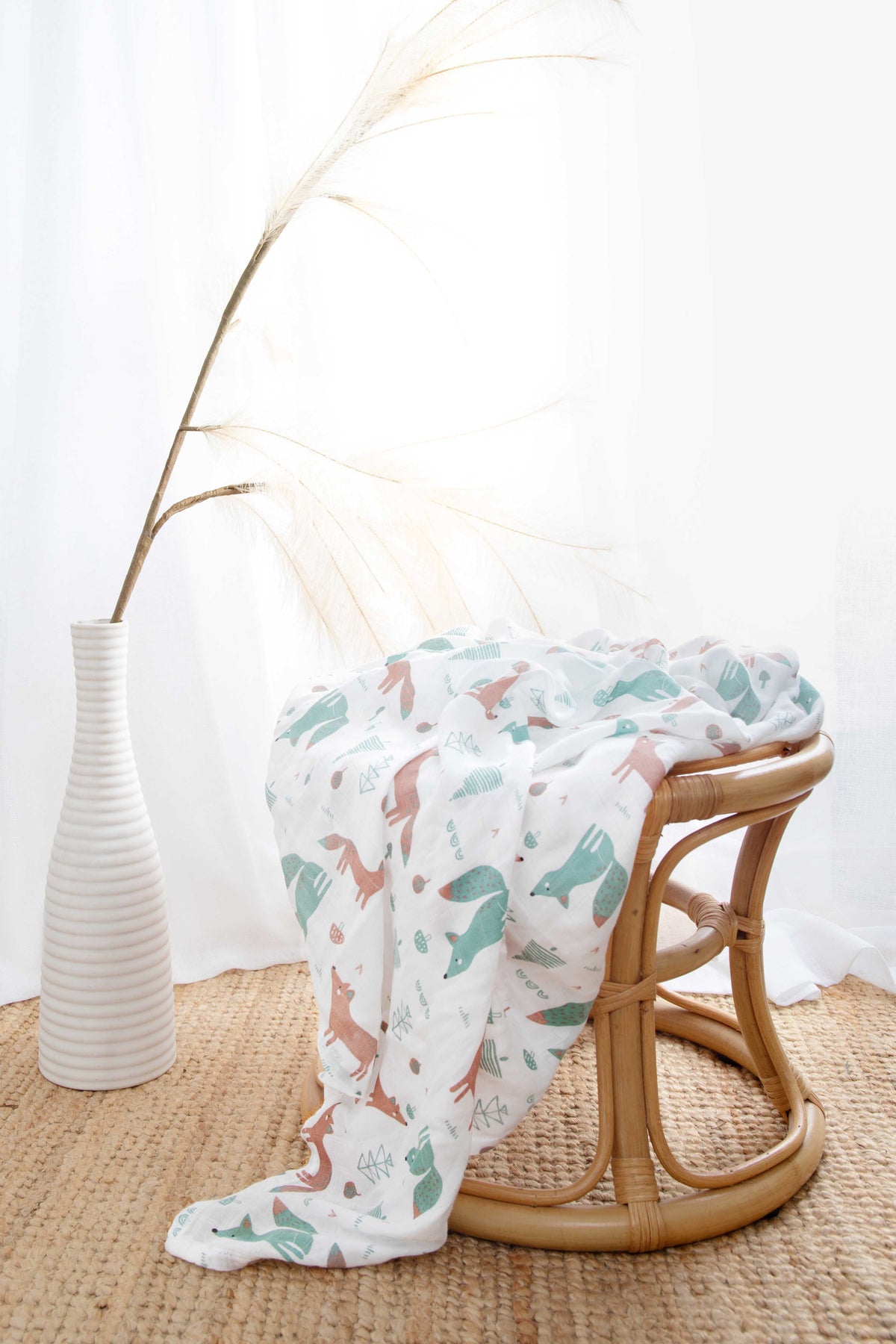 The fox-print muslin wrap draped over a rattan stool beside a white vase of pampas grass.