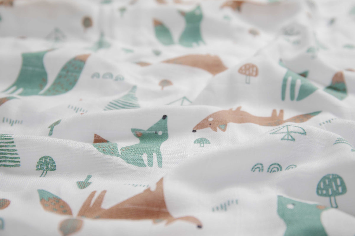 Close-up of the print: sage and terracotta foxes, small trees and mushrooms on white muslin.