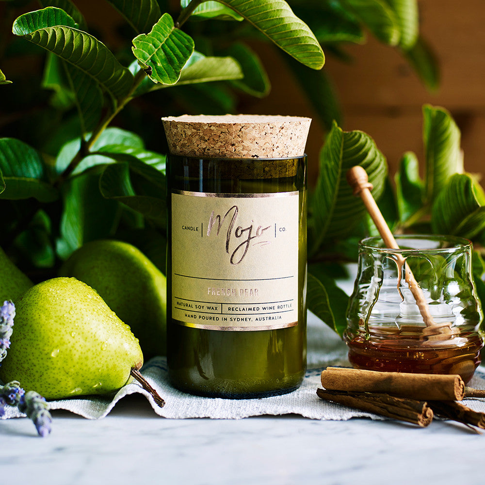 French Pear candle in a reclaimed wine bottle beside pears, honey and cinnamon sticks