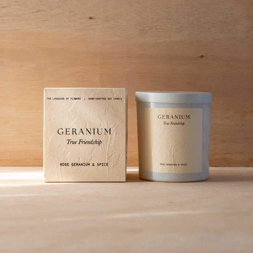 The Geranium candle in its white vessel beside its cream box.
