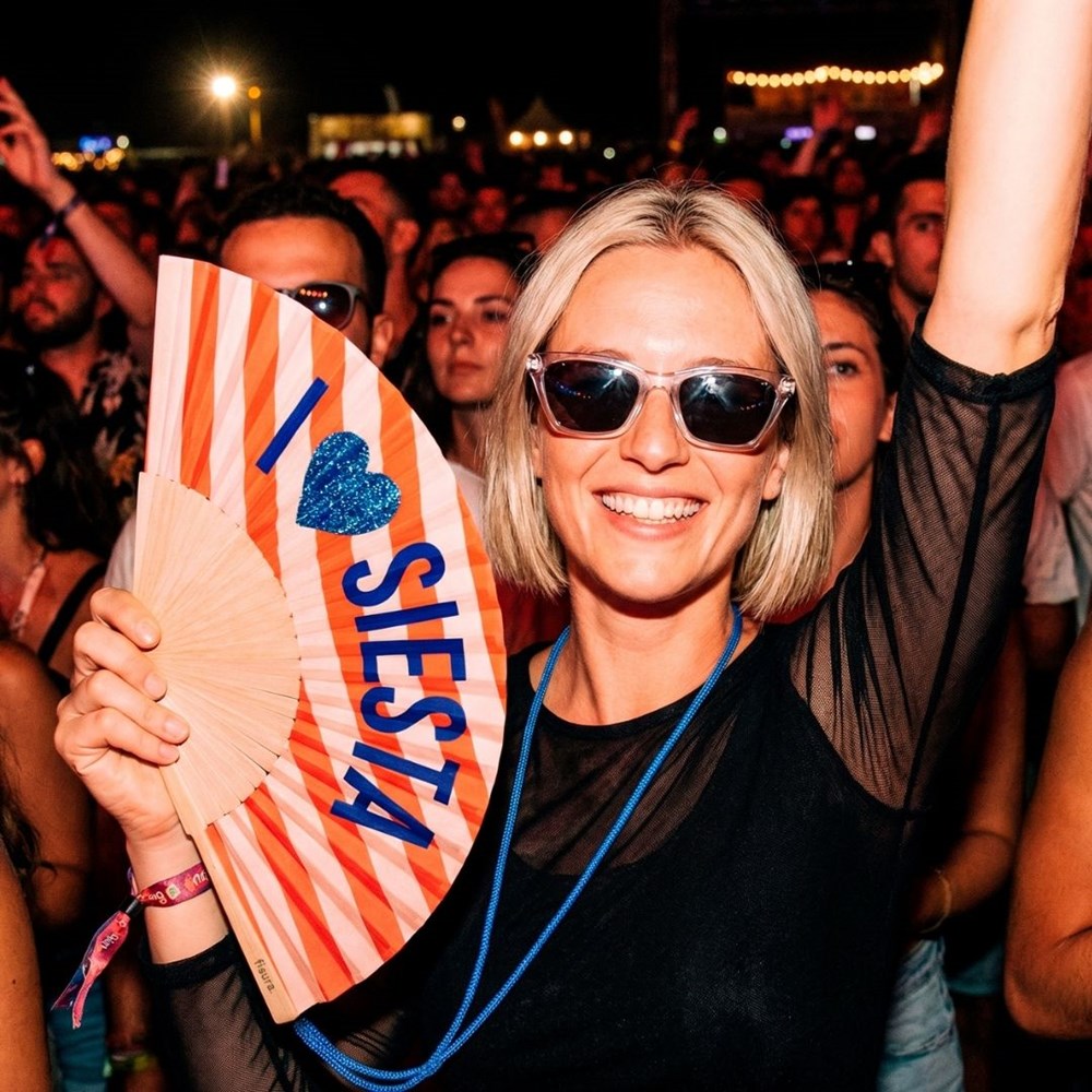 Woman in sunglasses at an evening concert holding up the I love Siesta fan