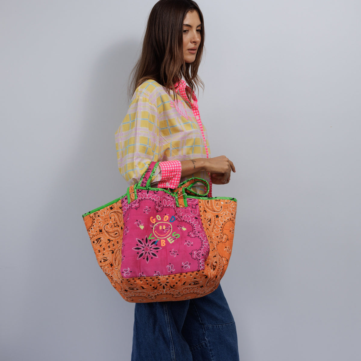 Woman carrying the quilted tote over her forearm by its short handles, with orange bandana-print sides and the hot pink Good Vibes front.