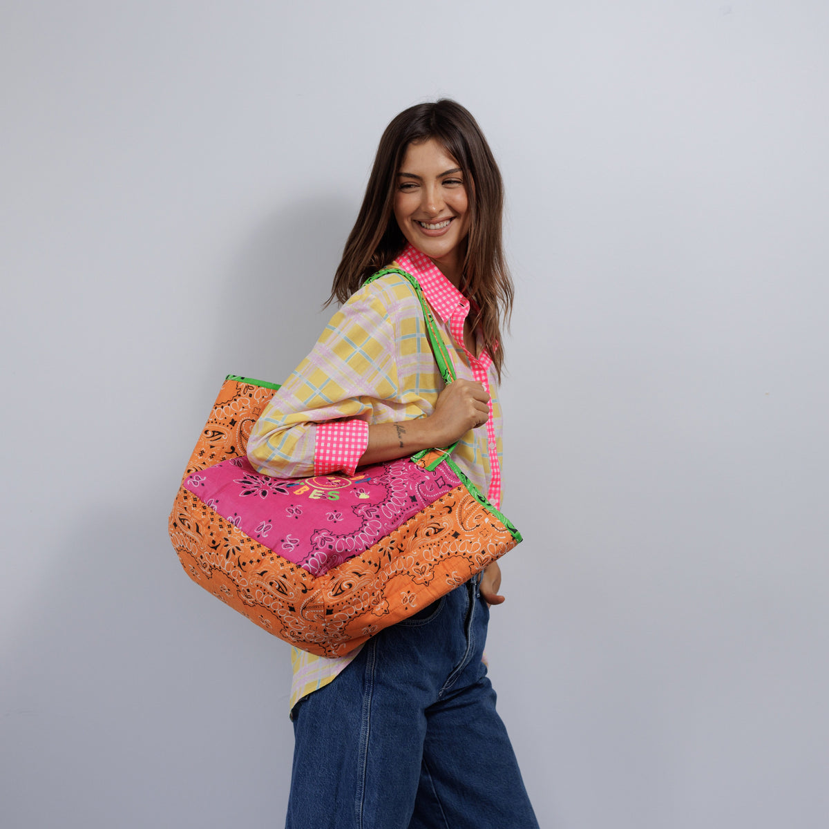 The orange and pink quilted tote worn over the shoulder on its long lime-trimmed handles.