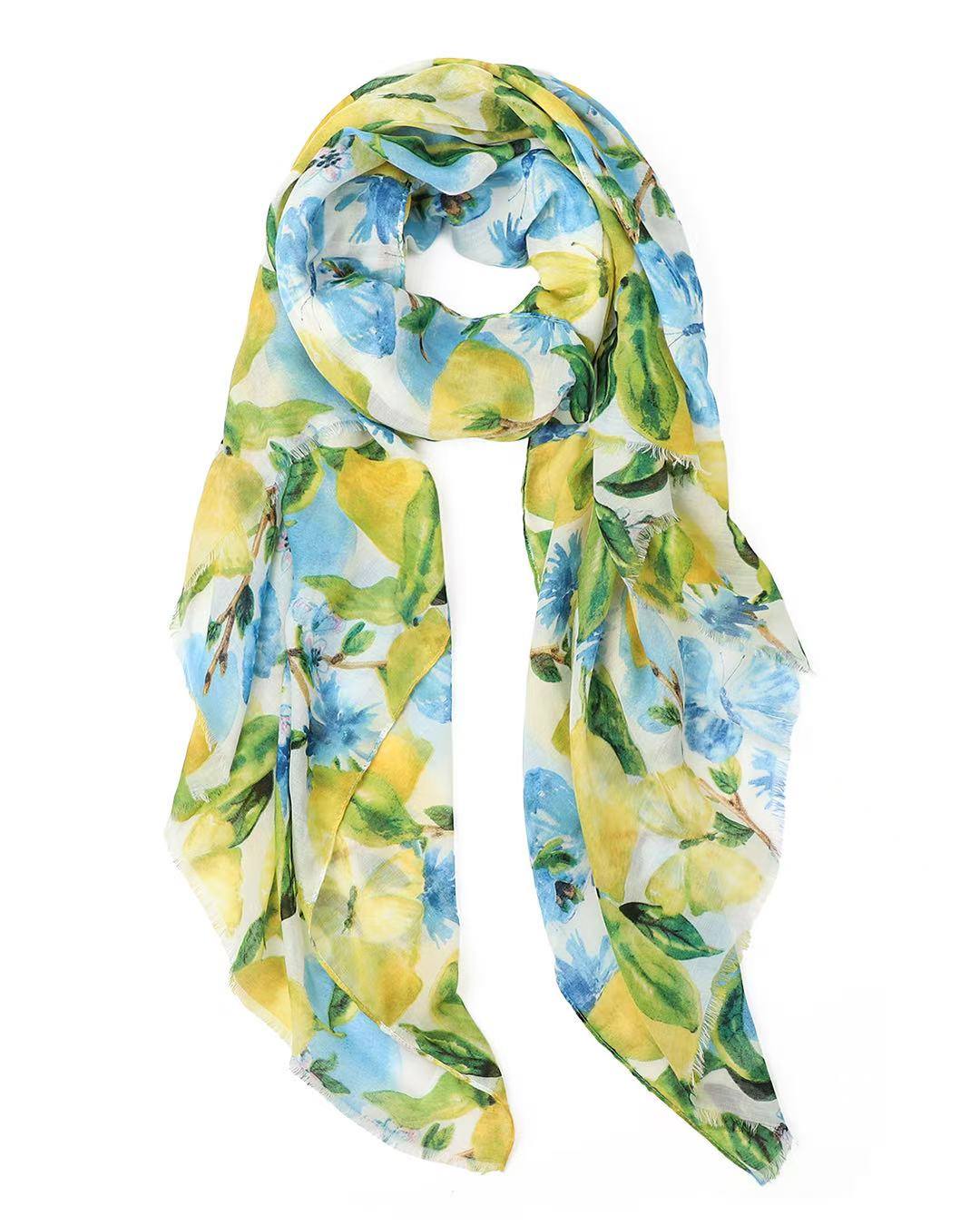 Lightweight white scarf printed with watercolour lemons, green leaves and blue blossoms, looped and hanging against a white background.