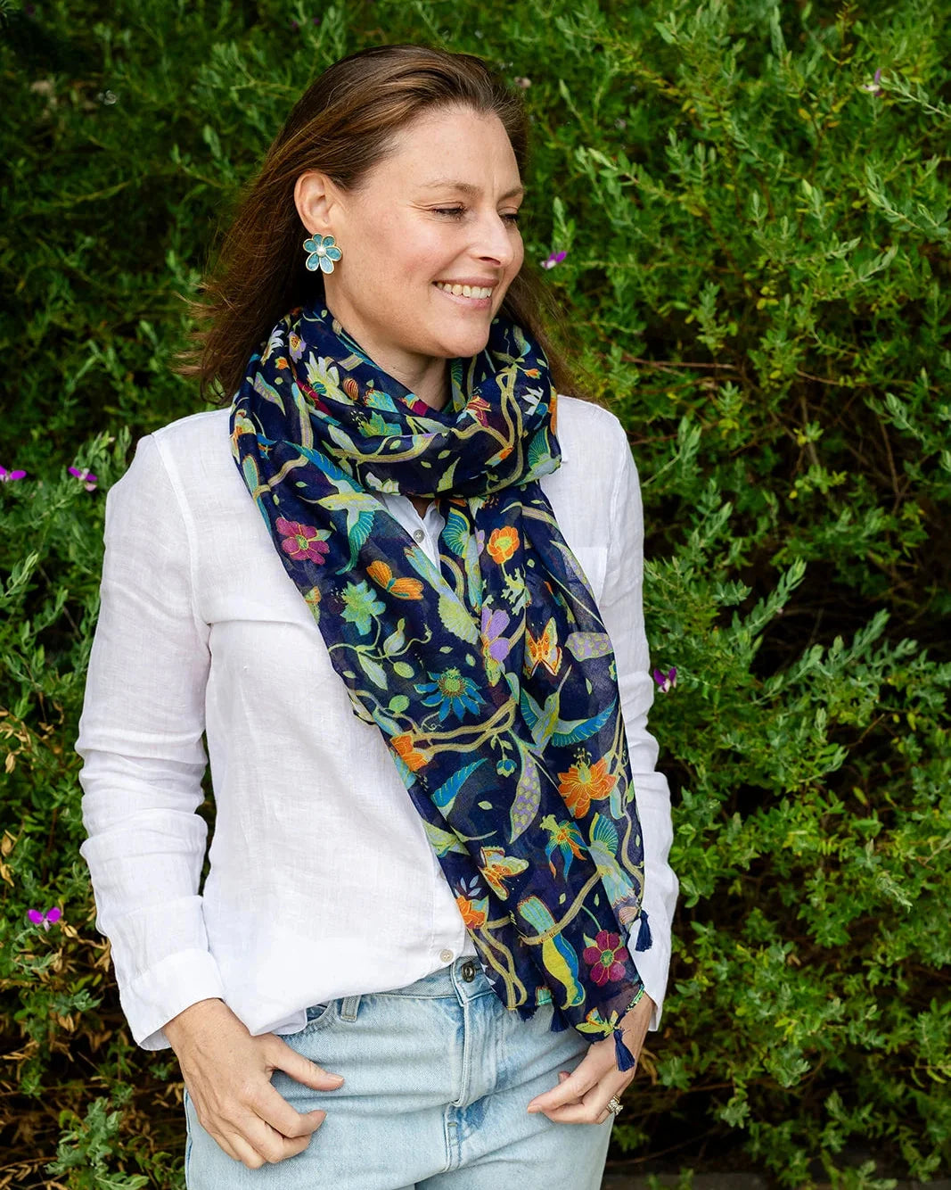 Woman in a white shirt wearing the navy botanical scarf draped long at her neck, standing in front of a green hedge.