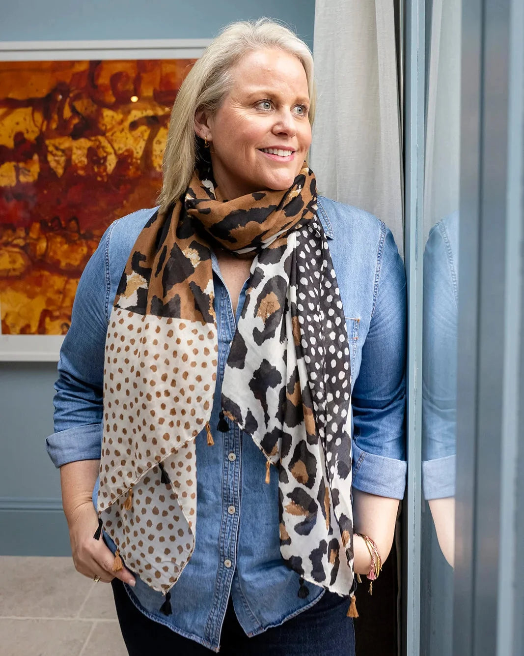Woman in a denim shirt wearing the leopard and spot scarf hanging long over a dark top.