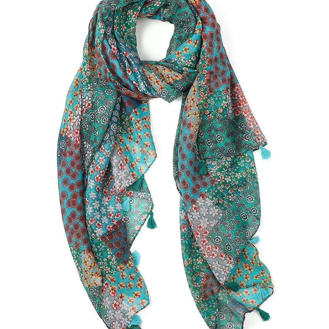 Lightweight scarf in a turquoise and green patchwork of small floral prints, looped to show the teal tassels.