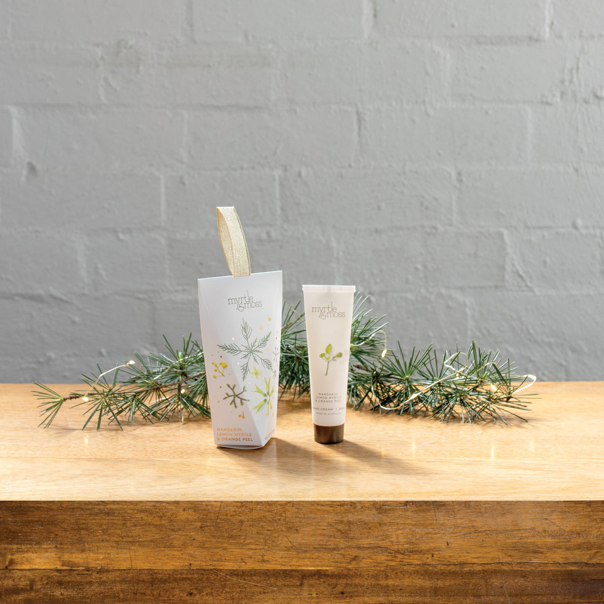The Citrus hanging hand cream box beside its 30 mL tube on a wooden table with pine sprigs.