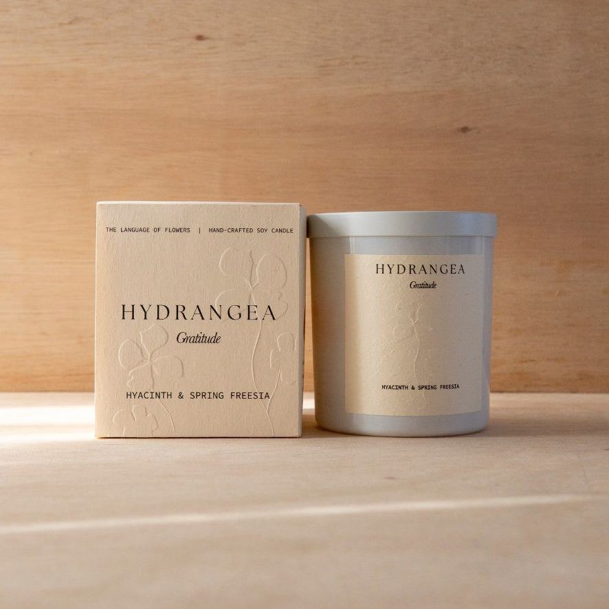 The Hydrangea candle in its white vessel beside its cream box.