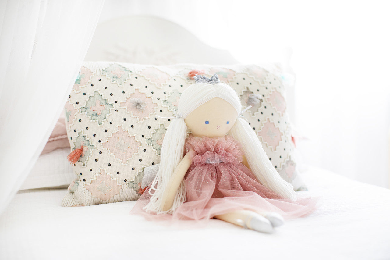 Penelope princess doll seated against cushions on a white bed