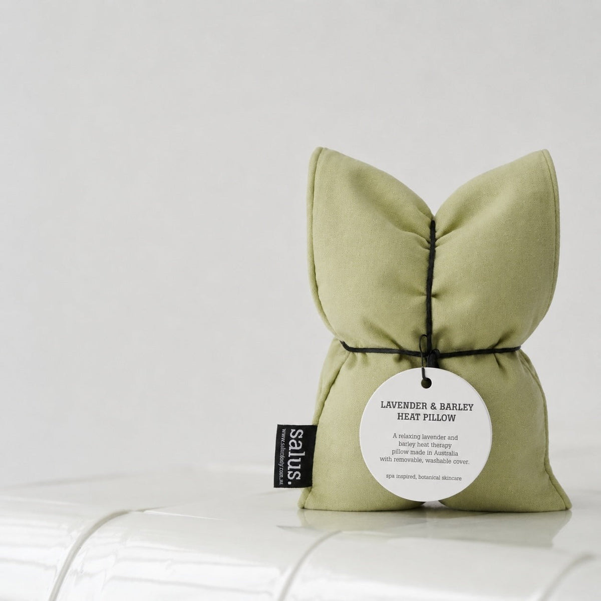 Mint Salus heat pillow standing on the edge of a white bath against a pale wall