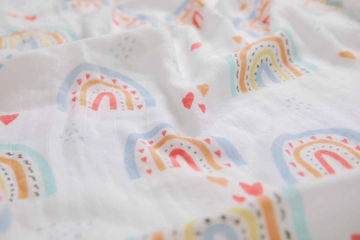 Close-up of the print: soft rainbows in blue, orange and red with tiny hearts on white muslin.