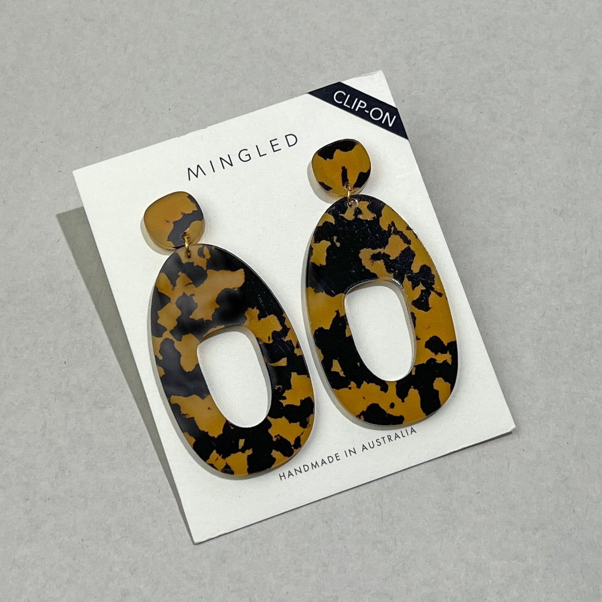 A pair of large tortoiseshell acrylic clip-on earrings on a white Mingled card marked Clip-On, each a wide open shape hung from a small rounded top.