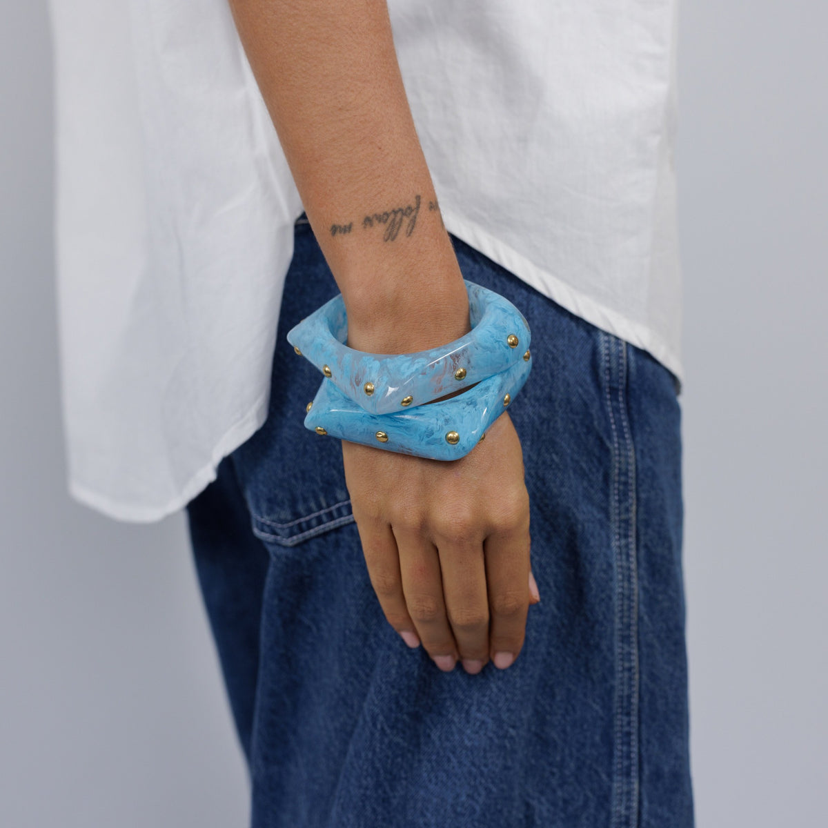 A model wearing two stacked blue studded bangles with jeans and a white shirt.