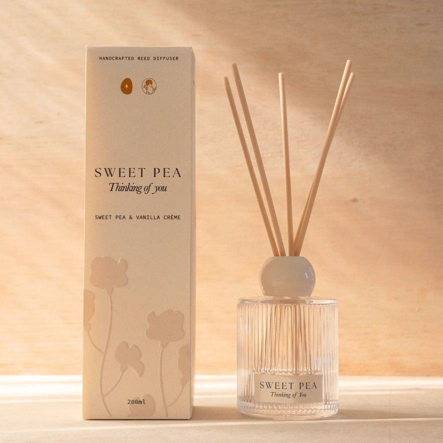 The Sweet Pea reed diffuser, a ribbed glass bottle with natural reeds, beside its cream box.