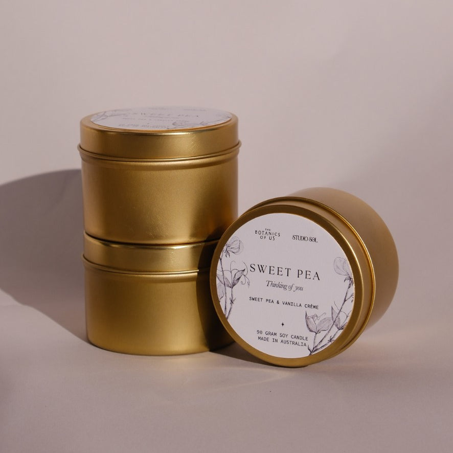 Three gold Sweet Pea travel tins, one tipped forward to show its lid label with a drawing of the sweet pea.