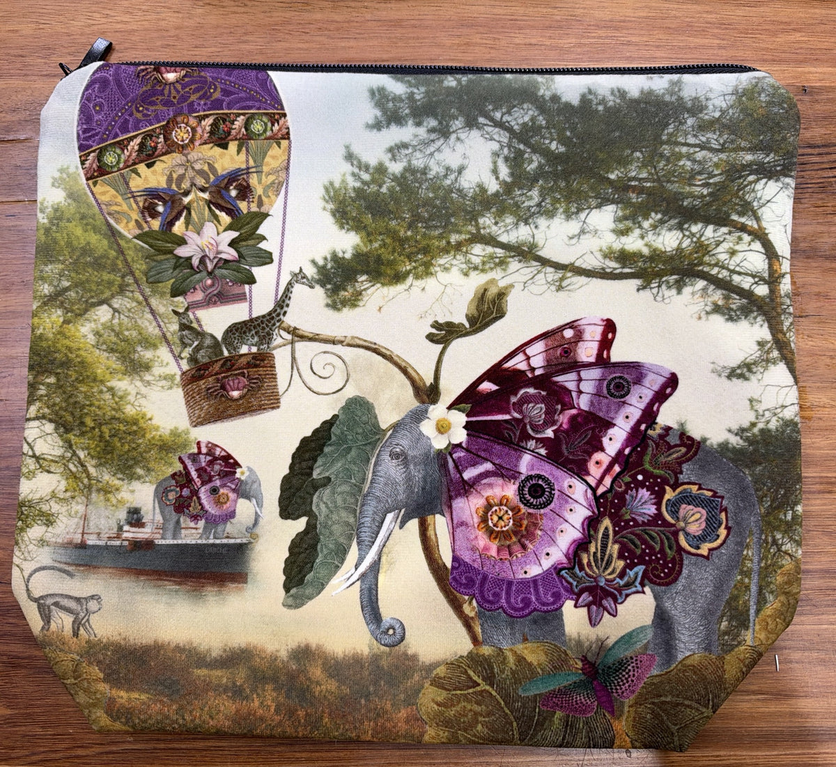 Velour cosmetic bag printed with Isabelle Frioux's Butterfly Elephant: an elephant with purple butterfly wings beside a hot-air balloon, with a black zip.