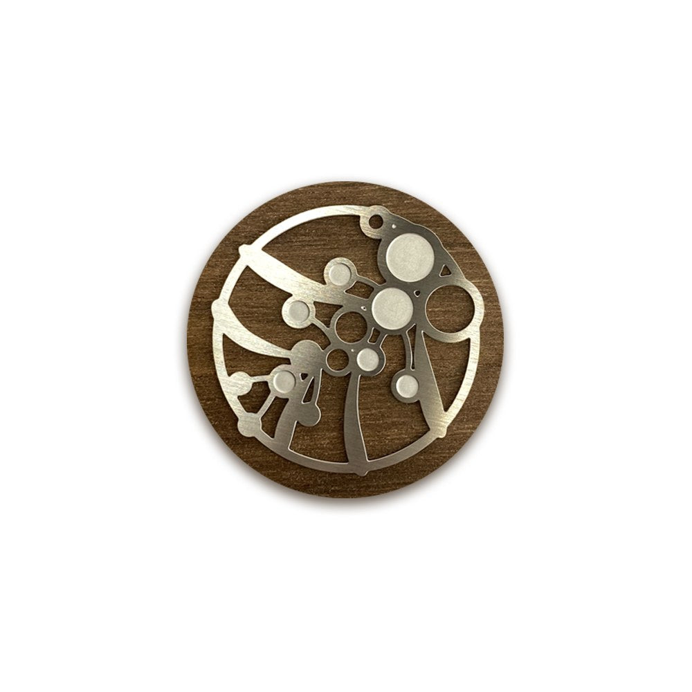 The round wattle brooch close up on white, silver steel wattle cut-outs on walnut timber.