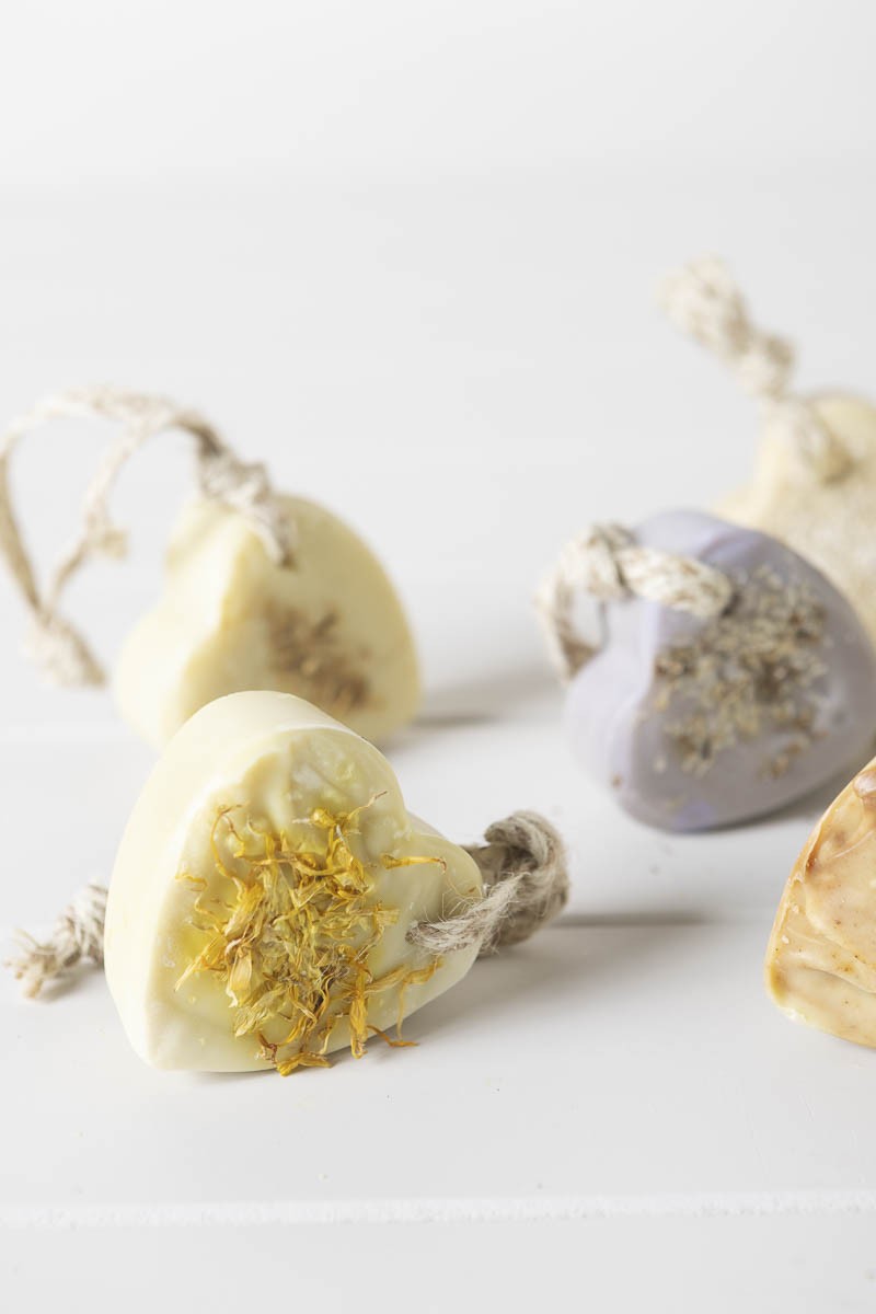 Several handmade heart soaps with jute loops, some topped with calendula petals and lavender buds