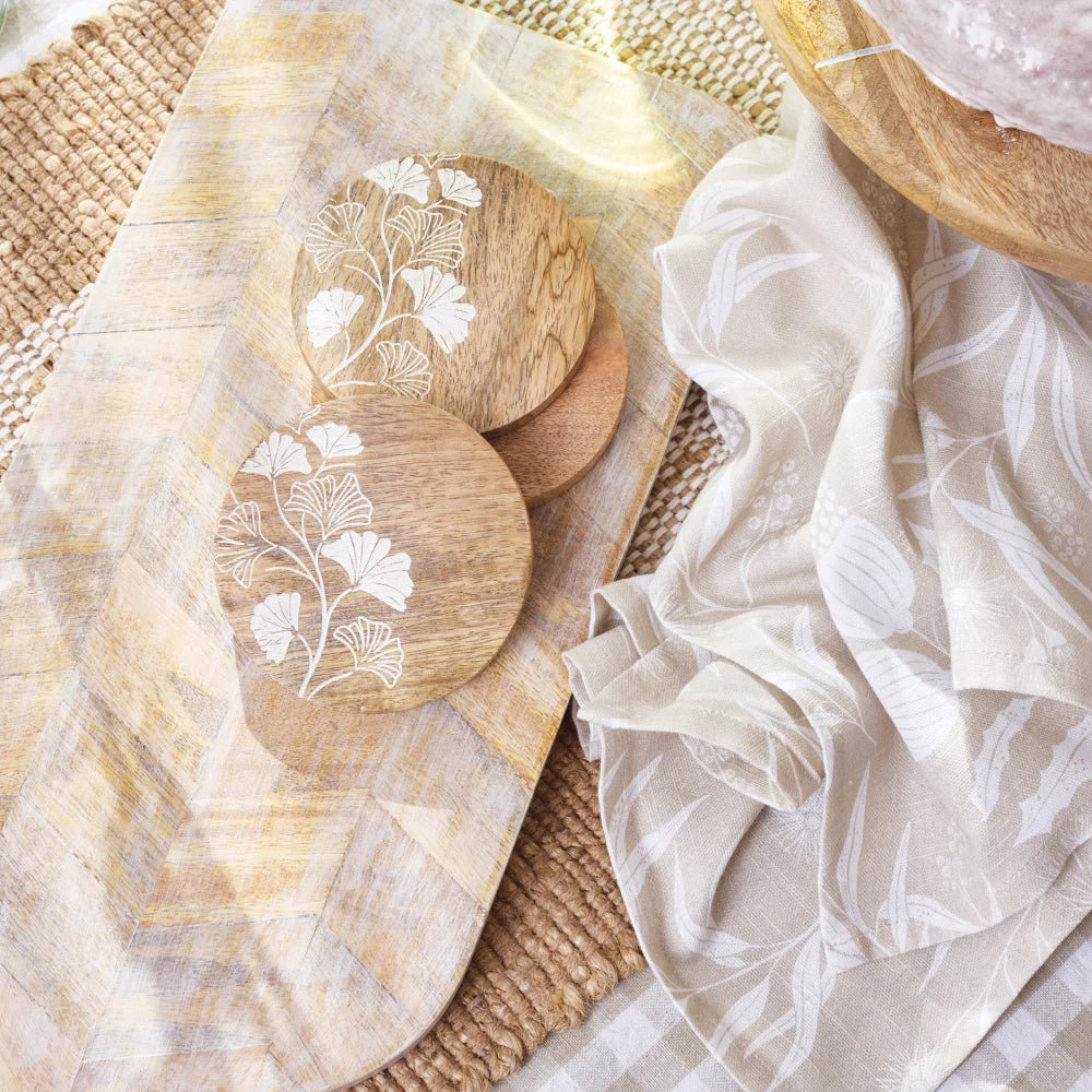 Bindi tea towel styled with mango wood serving boards and coasters on a woven mat