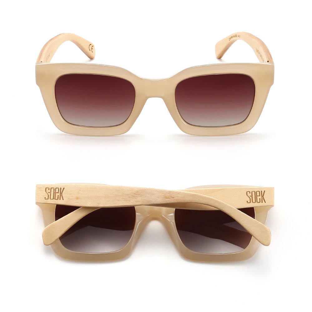 Two pairs of Zahra sunglasses in nude, one front-on and one folded, showing the pale wood arms