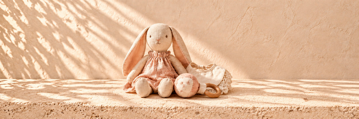 A linen plush bunny in a pink dress with a soft rattle and a lace-trimmed bib