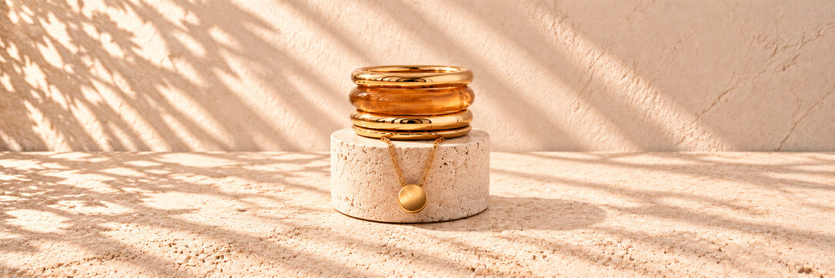 A stack of gold and honey resin bangles on a round limestone plinth, with a fine gold chain draped below