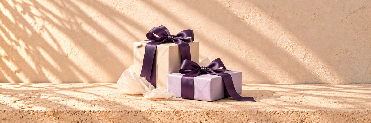 Two ivory and lavender parcels with purple satin bows and ivory tissue