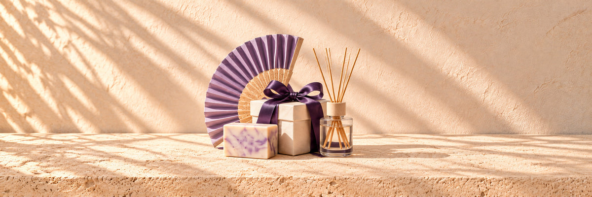 A purple hand fan, a bar of soap, a reed diffuser and a ribbon-tied gift box