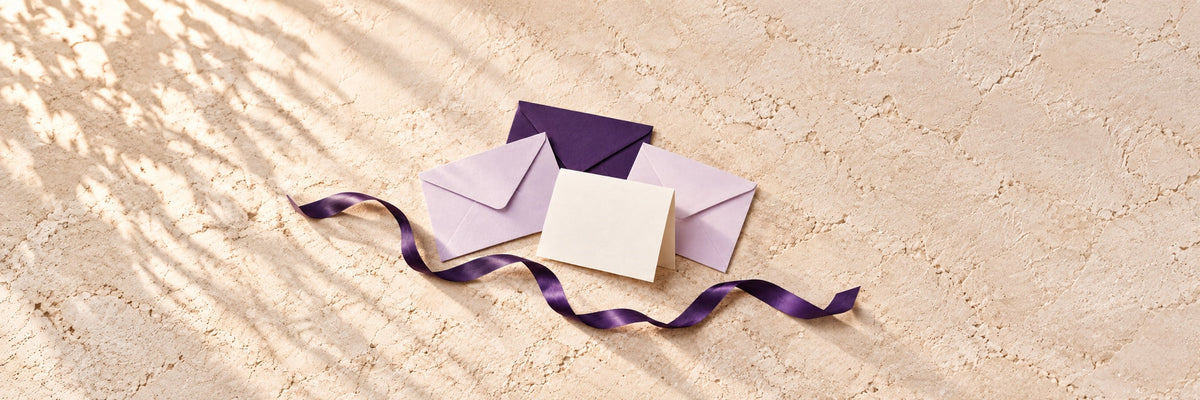 Blush pink envelopes on a white textured surface with a single pink carnation