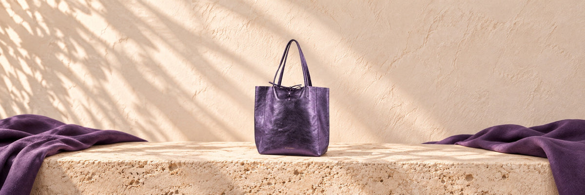 A tan croc-embossed handbag on a round plinth against a blush wall