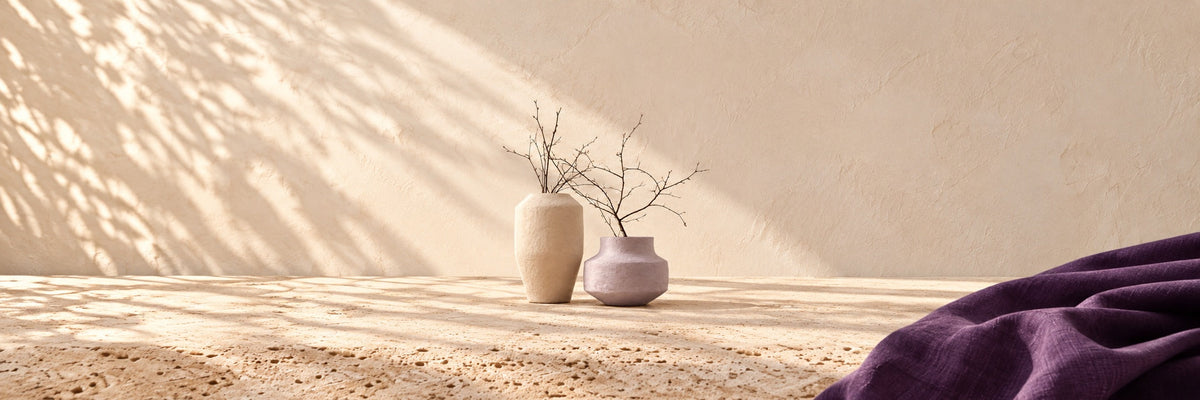 Two textured stone-coloured vases with bare branches by a sunlit window