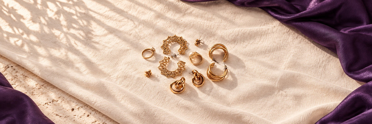 Gold statement earrings and rings scattered on soft linen