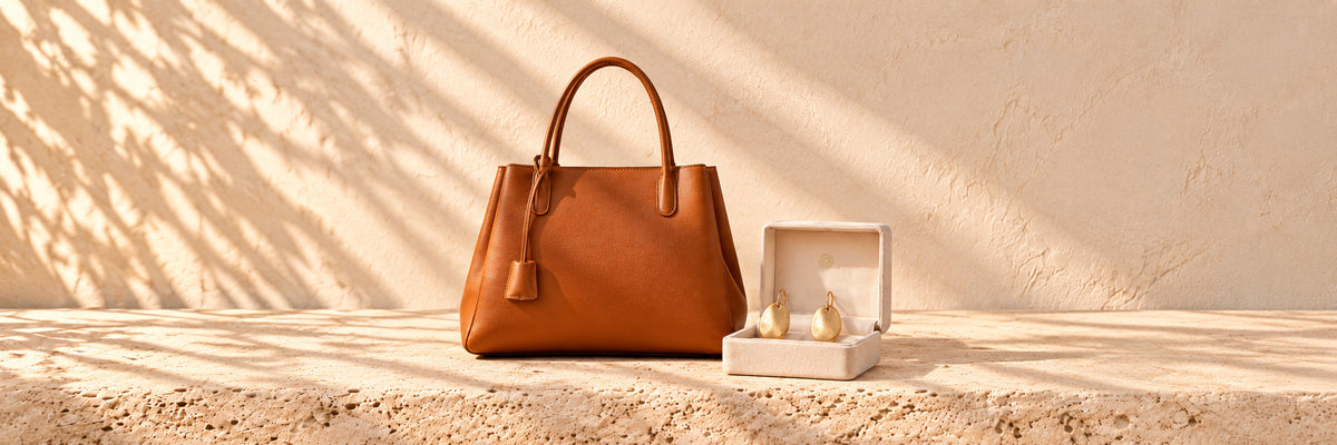 A tan leather handbag beside gold disc earrings in an open ivory jewellery box