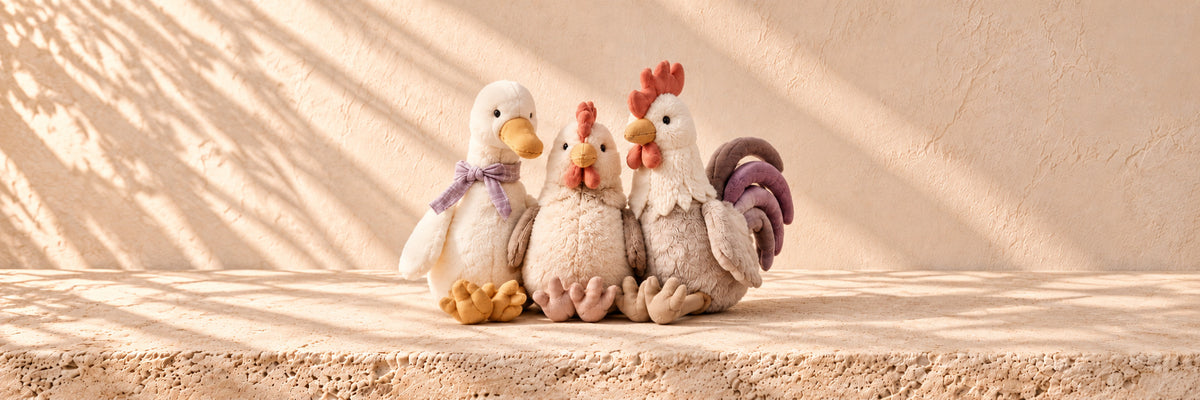 Three plush farm toys sitting together: a duck, a hen and a rooster
