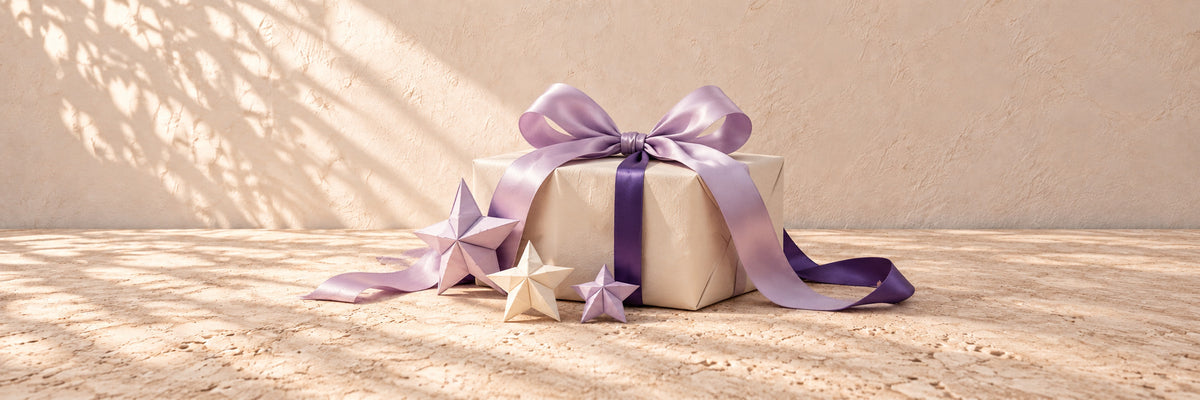 An ivory parcel with lavender satin and folded paper stars on pale limestone