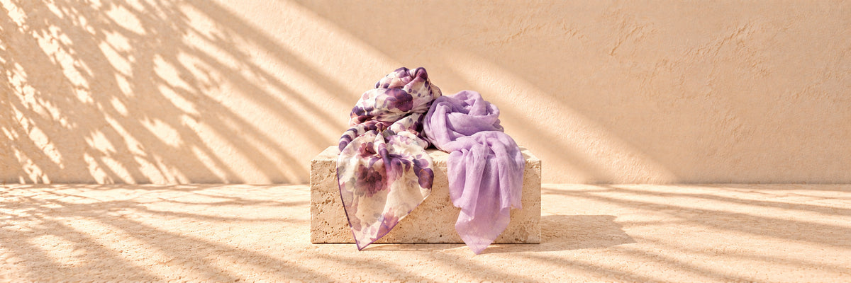 A floral print scarf and a lavender scarf draped over a limestone plinth